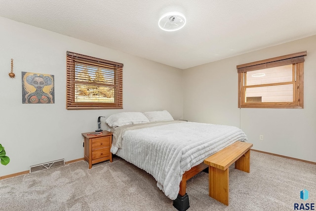 bedroom featuring a textured ceiling, baseboards, visible vents, and light carpet