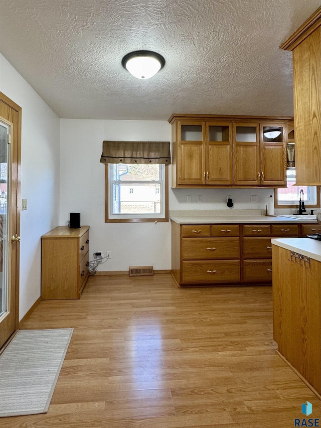 kitchen featuring brown cabinetry, light wood finished floors, light countertops, glass insert cabinets, and a wealth of natural light