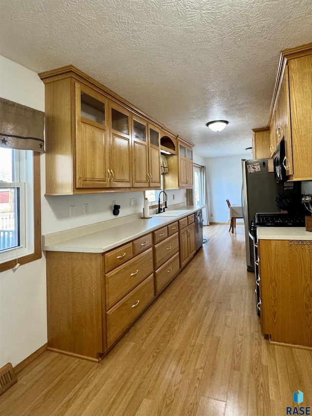 kitchen with brown cabinetry, light countertops, light wood-style floors, and a sink