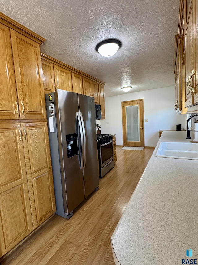 kitchen featuring light wood-type flooring, a sink, appliances with stainless steel finishes, brown cabinetry, and light countertops