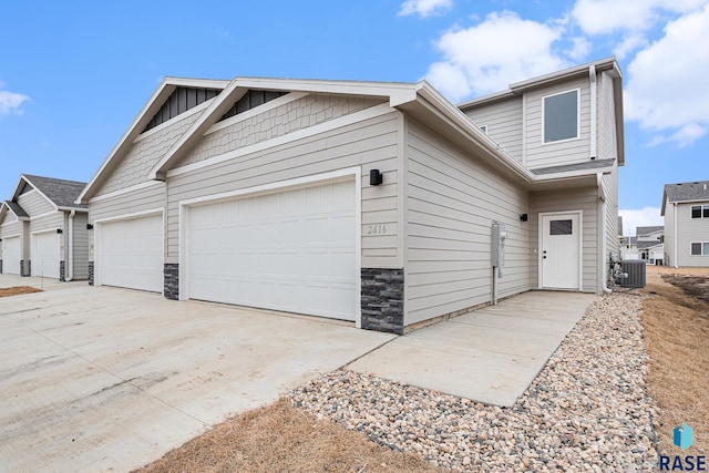 view of home's exterior with stone siding, driveway, central AC, and a garage