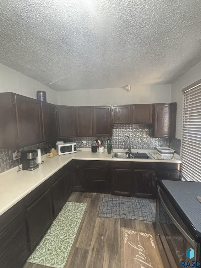 kitchen with a sink, backsplash, dark wood-style floors, light countertops, and range