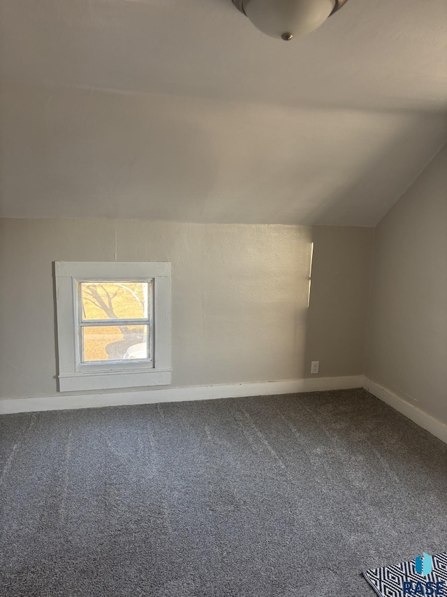 carpeted empty room featuring baseboards and vaulted ceiling