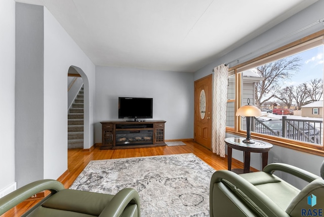 living room with arched walkways, stairs, baseboards, and wood finished floors