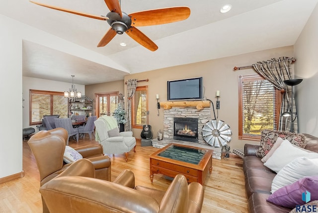 living room with ceiling fan with notable chandelier, wood finished floors, a fireplace, and vaulted ceiling