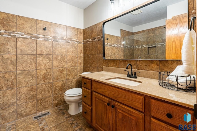 bathroom with vanity, visible vents, a tile shower, tile walls, and toilet