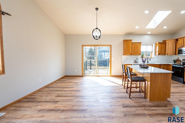 kitchen featuring light countertops, light wood-style floors, appliances with stainless steel finishes, lofted ceiling with skylight, and a center island