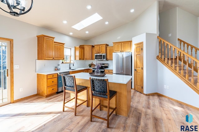 kitchen with a kitchen island, a skylight, a sink, light countertops, and appliances with stainless steel finishes