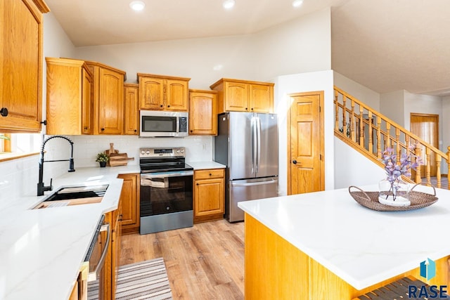 kitchen featuring a sink, decorative backsplash, vaulted ceiling, stainless steel appliances, and light wood-type flooring