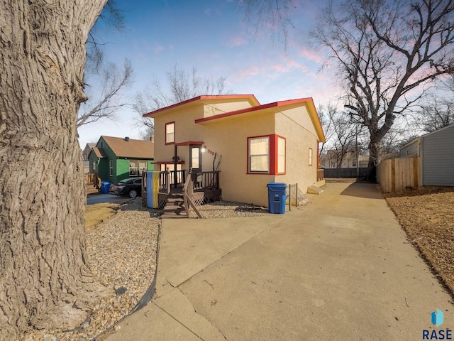 back of property at dusk featuring stucco siding, driveway, and fence