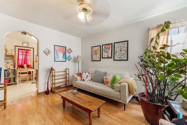 living room featuring arched walkways, light wood-style flooring, baseboards, and ceiling fan