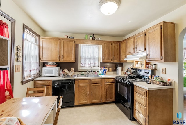 kitchen with black appliances, under cabinet range hood, a sink, arched walkways, and light countertops