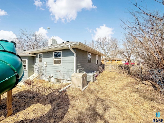 back of house featuring central AC unit, entry steps, a chimney, and fence