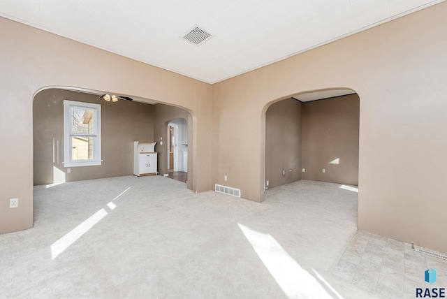 empty room with carpet flooring, visible vents, arched walkways, and ceiling fan