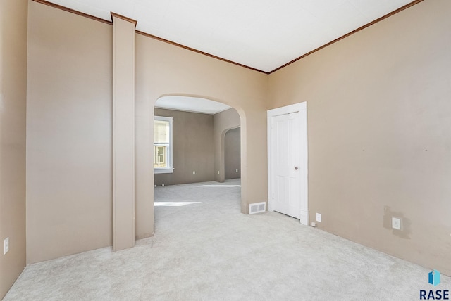 spare room featuring visible vents, arched walkways, light carpet, and crown molding