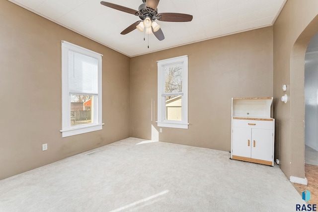 empty room featuring arched walkways, a healthy amount of sunlight, a ceiling fan, and light carpet