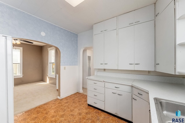 kitchen featuring a ceiling fan, arched walkways, a sink, light countertops, and white cabinets