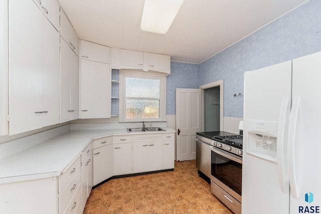 kitchen featuring stainless steel gas range, wallpapered walls, a sink, white cabinets, and white fridge with ice dispenser