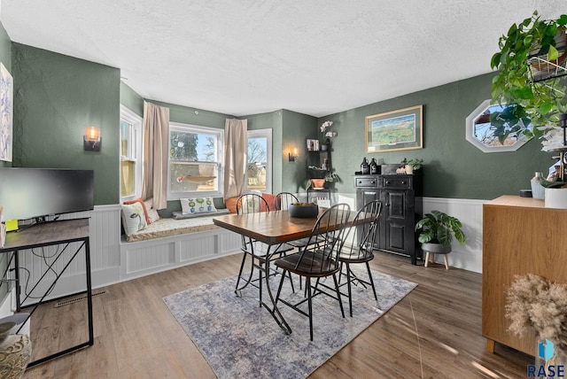 dining area with wood finished floors, a wainscoted wall, a textured wall, and a textured ceiling