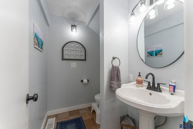 half bath featuring toilet, visible vents, baseboards, and a sink