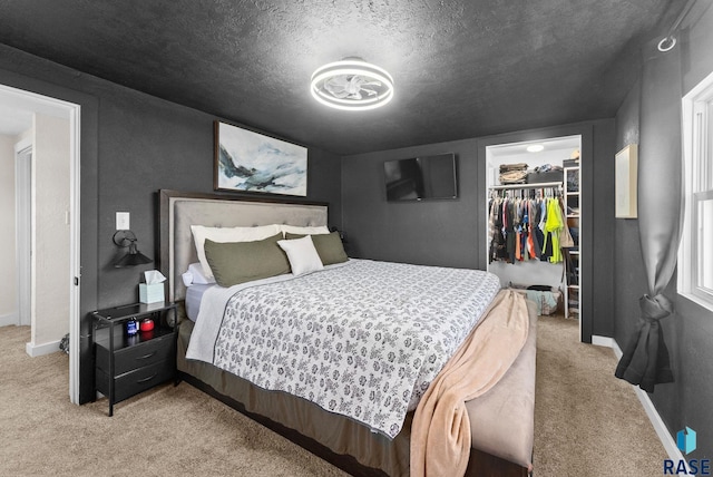 carpeted bedroom featuring a closet, a textured ceiling, a walk in closet, and baseboards