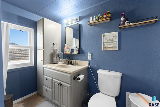 half bathroom featuring baseboards, toilet, a textured wall, tile patterned floors, and vanity