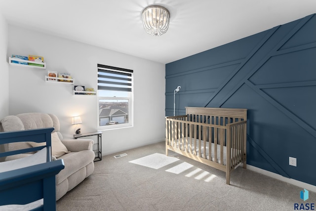 bedroom with visible vents, a crib, an inviting chandelier, carpet flooring, and a decorative wall