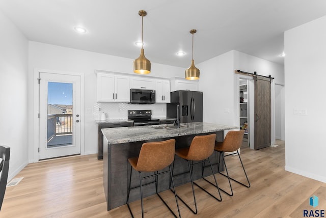 kitchen with a kitchen bar, a barn door, refrigerator with ice dispenser, range with electric stovetop, and white cabinetry