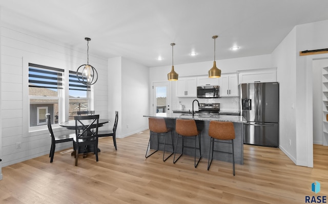 kitchen with a center island with sink, light wood-style flooring, stainless steel appliances, white cabinets, and a kitchen breakfast bar