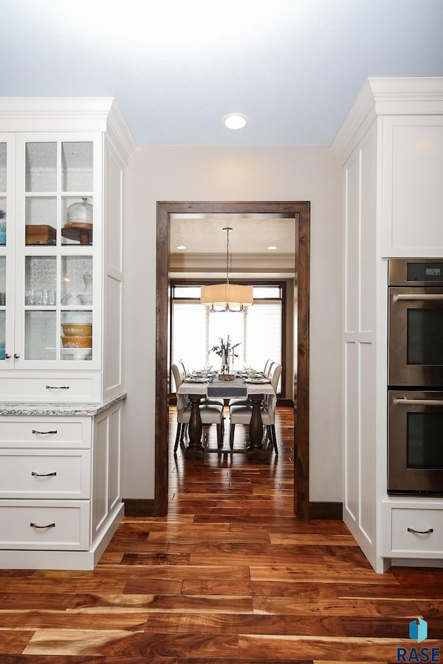 kitchen featuring light stone counters, stainless steel double oven, dark wood-style flooring, white cabinets, and glass insert cabinets