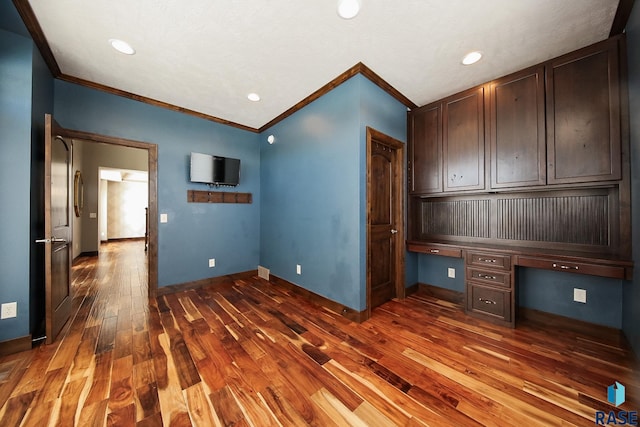 unfurnished office featuring baseboards, dark wood-style floors, crown molding, and built in study area