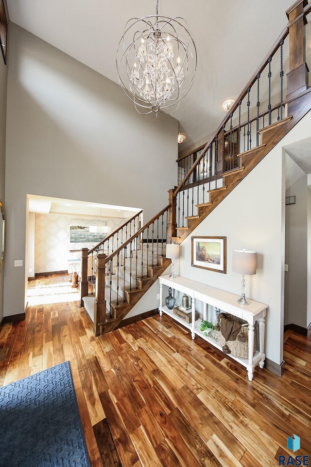 stairway with baseboards, a high ceiling, a chandelier, and hardwood / wood-style flooring