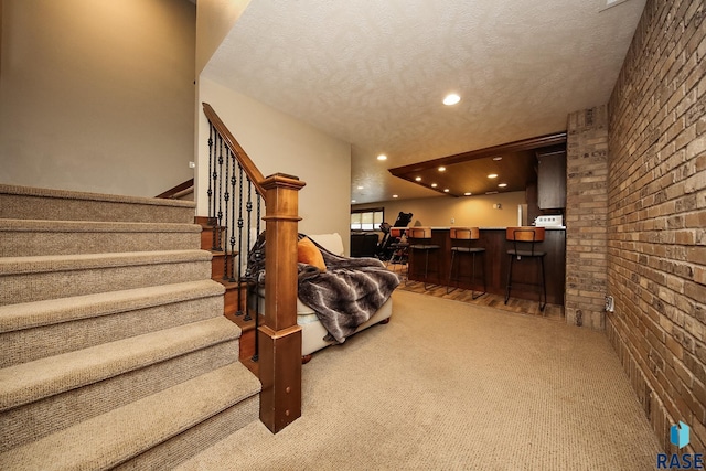 carpeted living area featuring brick wall, recessed lighting, stairs, a textured ceiling, and indoor bar