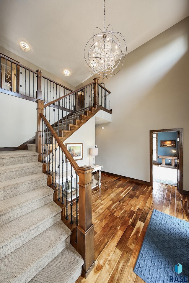 stairs featuring hardwood / wood-style flooring, baseboards, a towering ceiling, and a chandelier