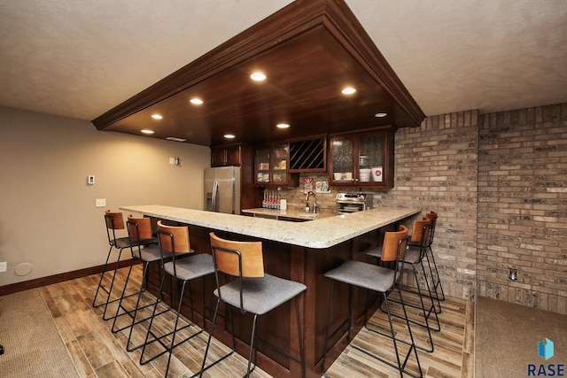 bar featuring brick wall, indoor wet bar, light wood-style flooring, stainless steel fridge, and a sink