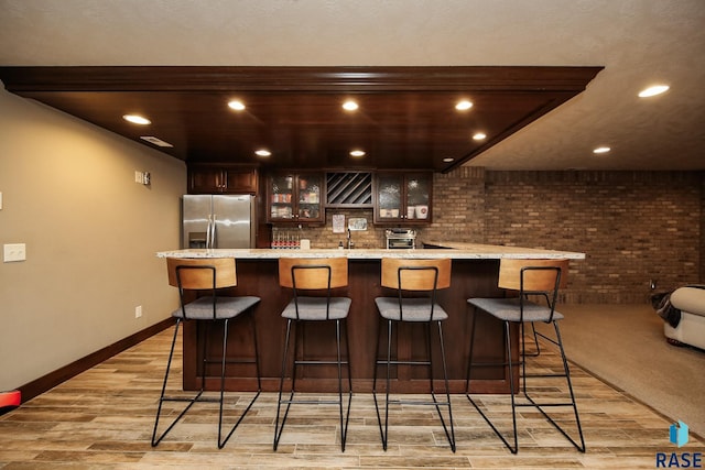 bar featuring brick wall, light wood finished floors, wet bar, stainless steel fridge with ice dispenser, and recessed lighting