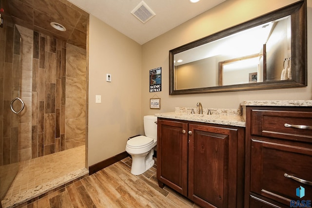 full bathroom with vanity, wood finished floors, visible vents, tiled shower, and toilet