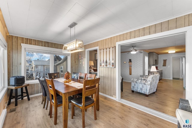 dining room featuring visible vents, light wood-style flooring, and wood walls