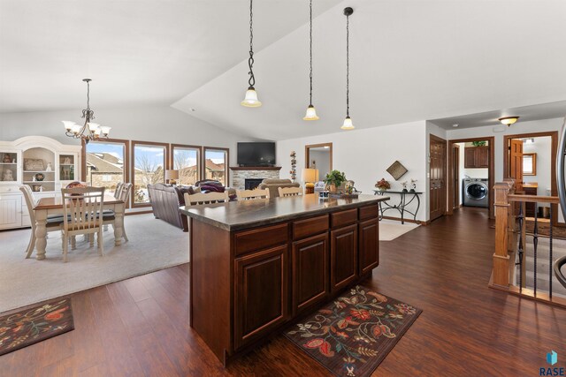 kitchen with dark wood-style floors, washer / dryer, a fireplace, hanging light fixtures, and dark countertops