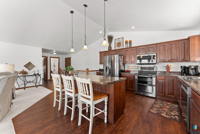 kitchen with a breakfast bar, dark wood finished floors, stainless steel appliances, dark countertops, and a center island