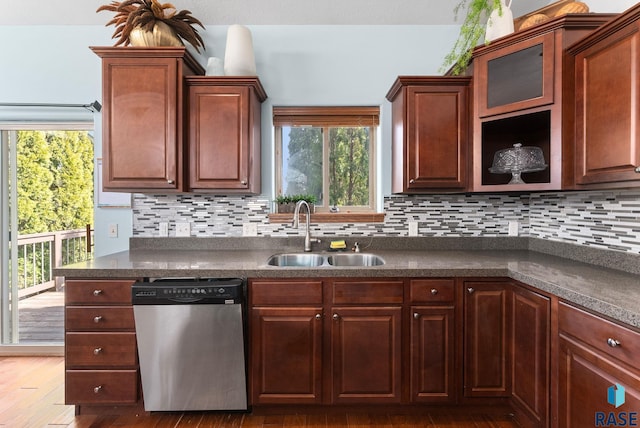 kitchen with stainless steel dishwasher, dark countertops, backsplash, and a sink