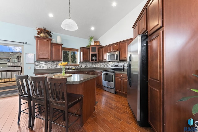 kitchen with a breakfast bar area, decorative backsplash, dark wood-type flooring, appliances with stainless steel finishes, and dark countertops