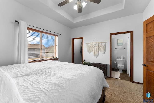 bedroom featuring ensuite bath, a tray ceiling, carpet flooring, and ceiling fan