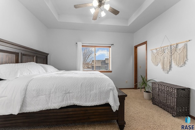 bedroom with a raised ceiling, light colored carpet, baseboards, and ceiling fan