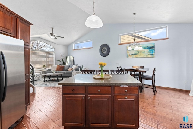 kitchen with pendant lighting, ceiling fan with notable chandelier, dark countertops, wood finished floors, and stainless steel fridge