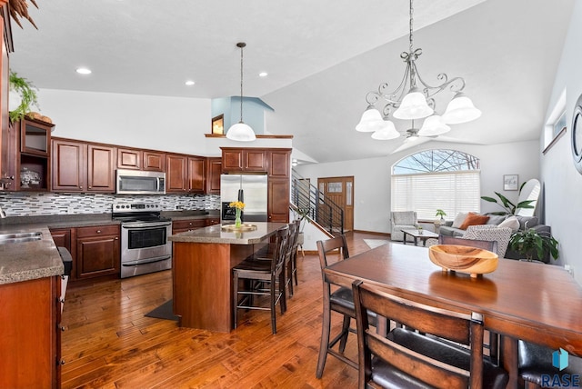 kitchen featuring a kitchen island, dark wood-style flooring, appliances with stainless steel finishes, tasteful backsplash, and a chandelier