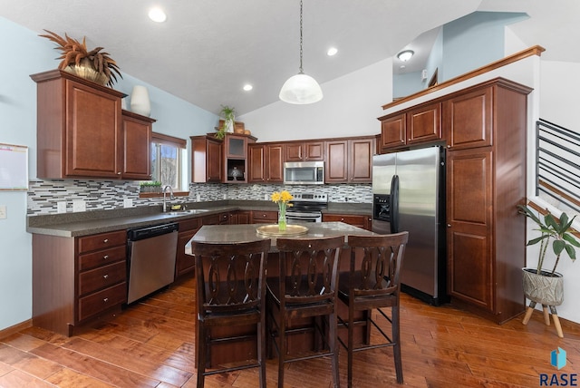 kitchen with a sink, a kitchen breakfast bar, dark countertops, dark wood finished floors, and stainless steel appliances