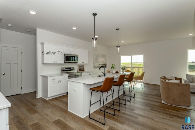 kitchen with wood finished floors, white cabinetry, stainless steel appliances, and a sink