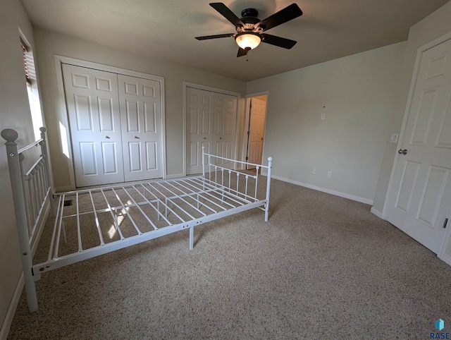 unfurnished bedroom featuring ceiling fan, baseboards, two closets, and carpet floors