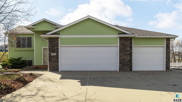 view of front of home with stone siding, driveway, a shingled roof, and a garage